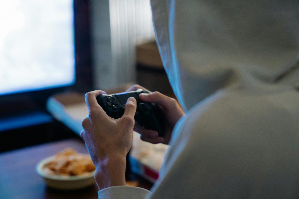 A young adult wearing a hoodie engages in gaming on a console at home for relaxation.