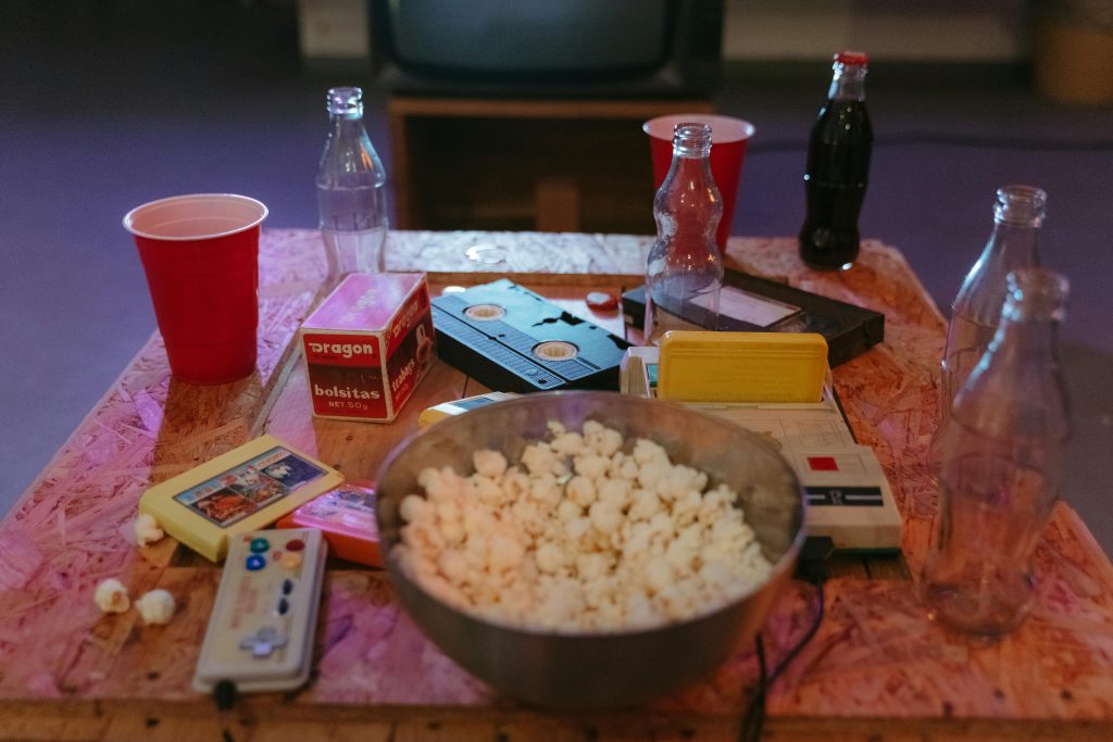A nostalgic setup with popcorn, VHS tapes, and retro gaming consoles on a wooden table.